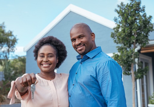 A happy couple stand in front of their new home, holding the house keys.