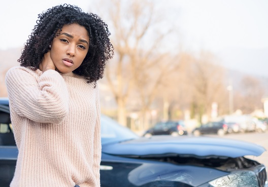 A woman holds her neck and stands next to her car after being involved in an accident.