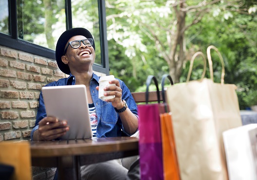 A Ghanaian man smiles and enjoys a coffee outdoors.