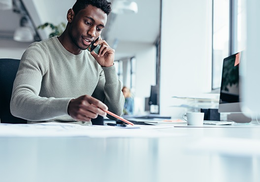 A Ghanaian man works through financial education material at his desk and speaks on his phone.