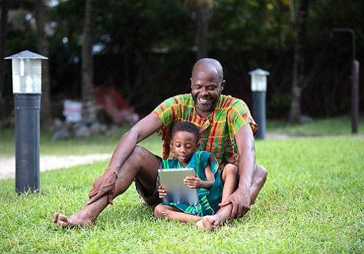 A Ghanaian father and son sit outdoors and read together.