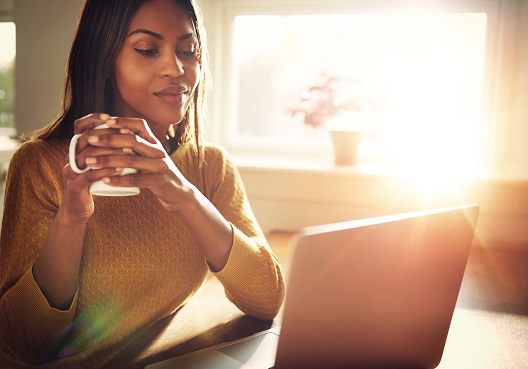 A Ghanaian woman holds a coffee cup and goes online to look up her closest Old Mutual branch.