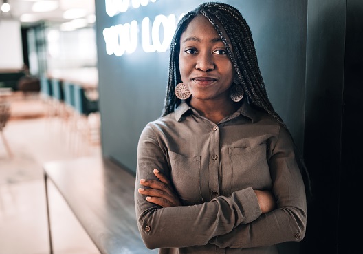 A woman folds her arms and smiles at her place of work.