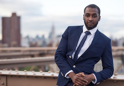A financial adviser wearing a dark blue suit stands outside of his office.