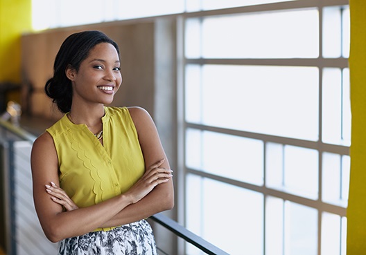 A woman with her arms folded smiles at her place of work.